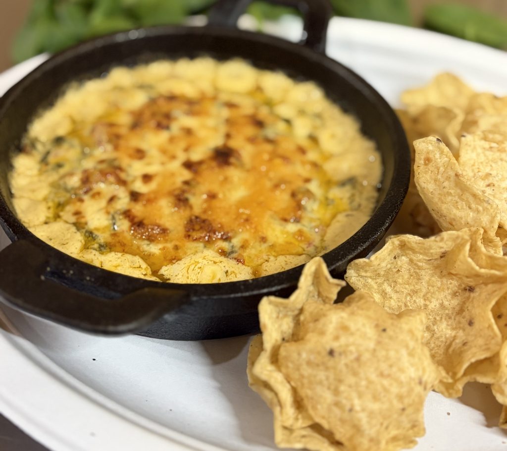 Creamy spinach blended with melted cheese in a cast iron pan with tortilla chips surrounding the pan.